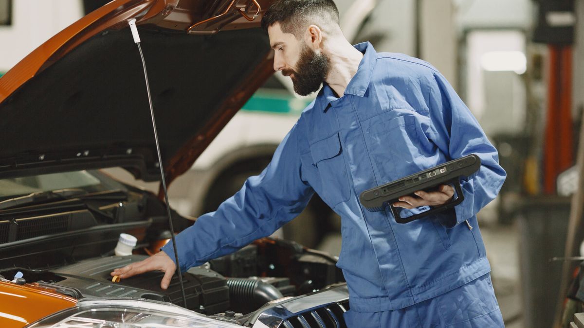 Un mécanicien contrôle le moteur d'une voiture d'occasion, tablette de diagnostic en main